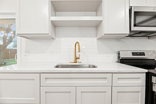 kitchen with stainless steel appliances, a sink, white cabinetry, light stone counters, and backsplash