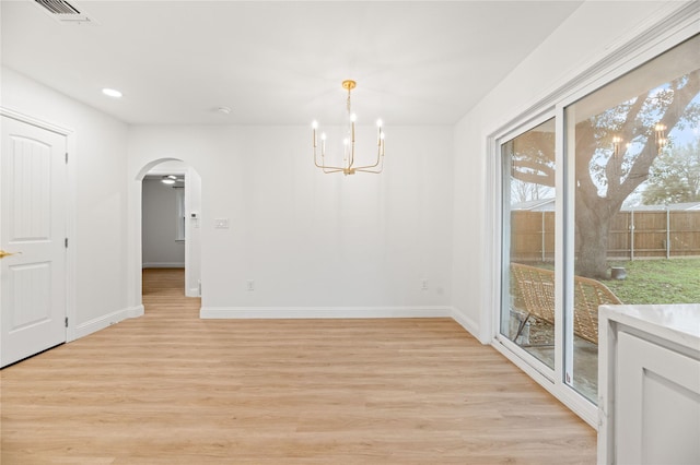 unfurnished dining area with baseboards, visible vents, arched walkways, a notable chandelier, and light wood finished floors