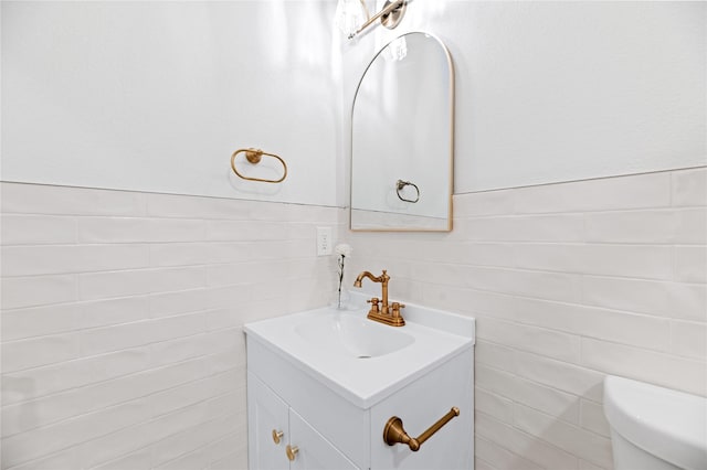 half bath featuring vanity, toilet, tile walls, and a wainscoted wall