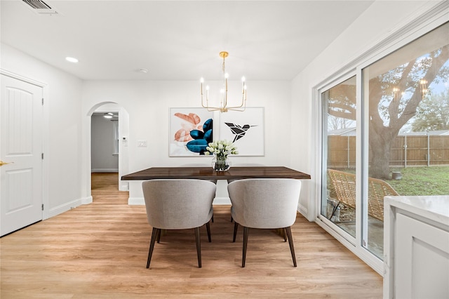 dining room with visible vents, light wood finished floors, baseboards, arched walkways, and a notable chandelier