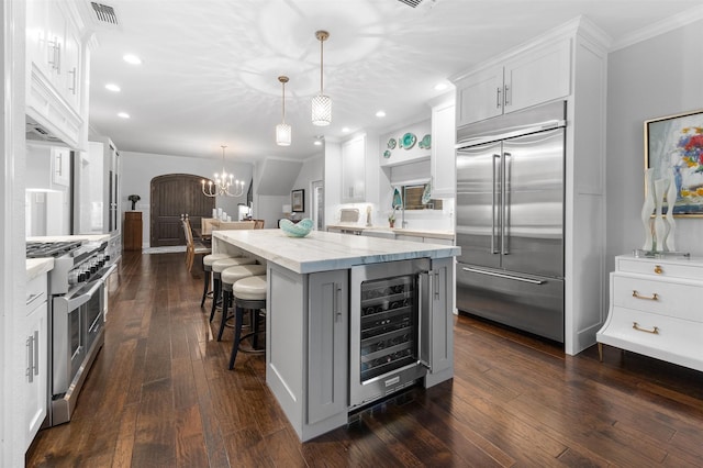 kitchen featuring light stone counters, high end appliances, white cabinets, beverage cooler, and pendant lighting