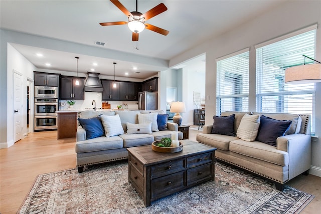 living room with light wood-type flooring, sink, and ceiling fan