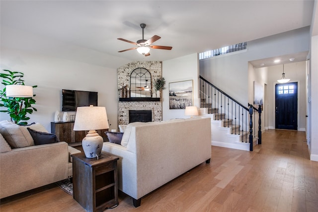 living room featuring ceiling fan, light hardwood / wood-style floors, a stone fireplace, and lofted ceiling