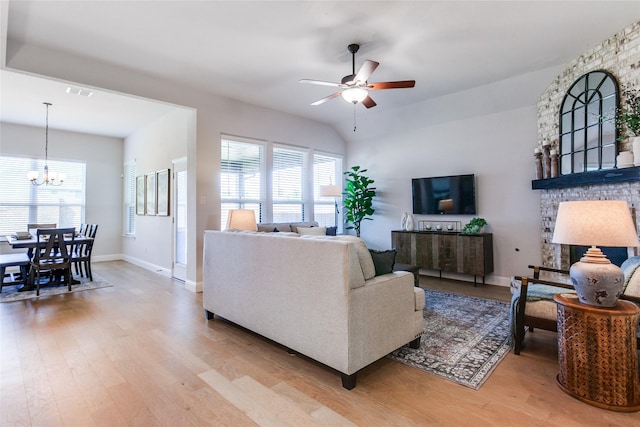 living room featuring ceiling fan with notable chandelier, light hardwood / wood-style floors, lofted ceiling, and a fireplace