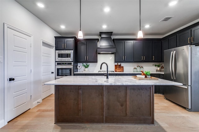 kitchen featuring light wood-type flooring, appliances with stainless steel finishes, light stone counters, and pendant lighting