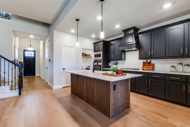 kitchen featuring a center island with sink, hanging light fixtures, stainless steel appliances, and custom range hood