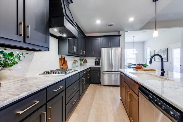 kitchen with light hardwood / wood-style flooring, stainless steel appliances, light stone countertops, pendant lighting, and sink