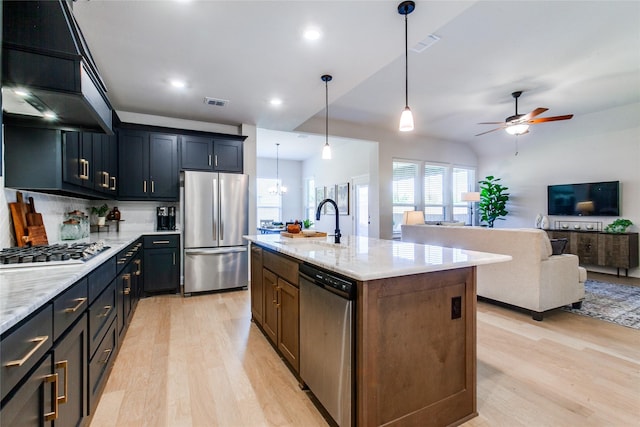 kitchen featuring a center island with sink, decorative light fixtures, light stone countertops, sink, and appliances with stainless steel finishes