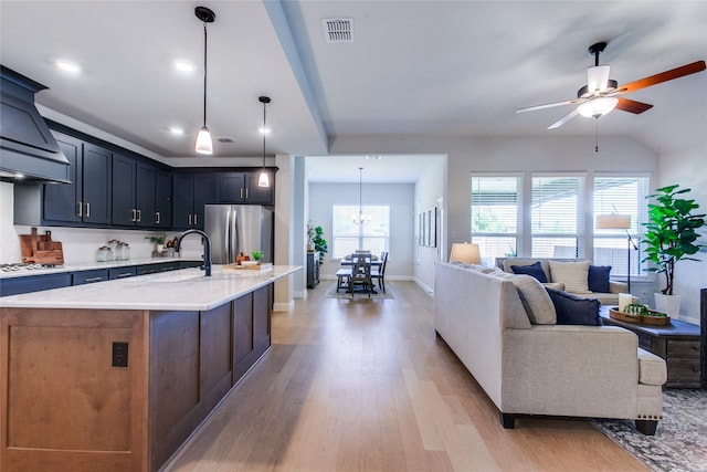 kitchen with an island with sink, hanging light fixtures, light hardwood / wood-style flooring, white gas stovetop, and stainless steel refrigerator