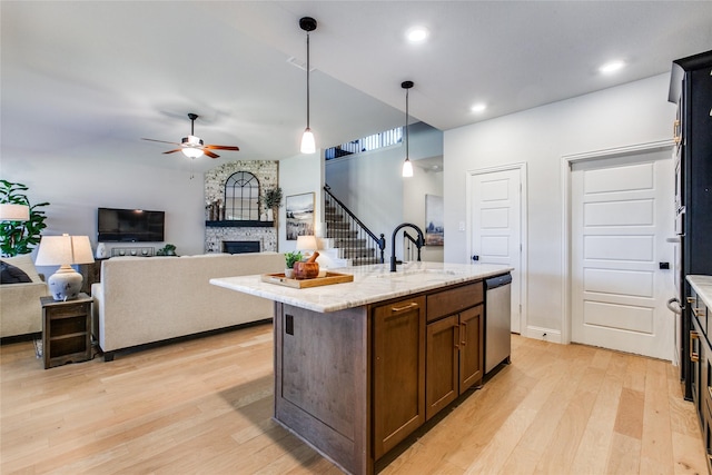 kitchen featuring dishwasher, light wood-type flooring, decorative light fixtures, sink, and a kitchen island with sink