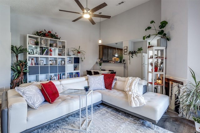 living area with a towering ceiling, ceiling fan, visible vents, and wood finished floors