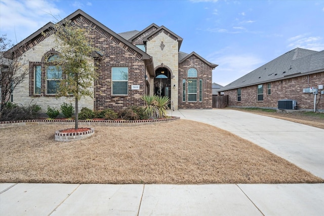 french country home featuring stone siding, central AC, and brick siding