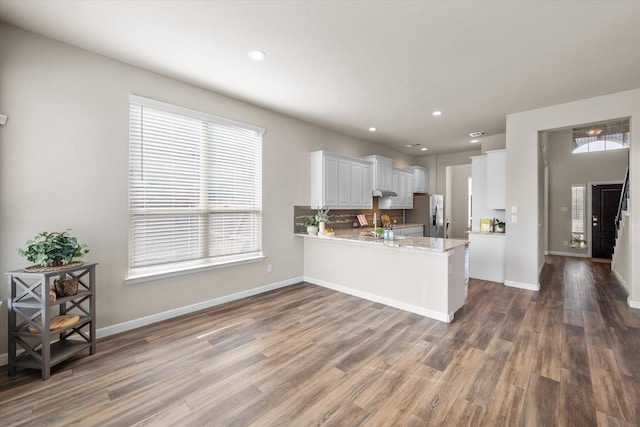 kitchen with a peninsula, stainless steel fridge, white cabinetry, and wood finished floors