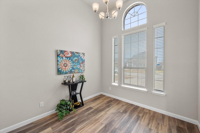 unfurnished room with a notable chandelier, wood finished floors, and baseboards