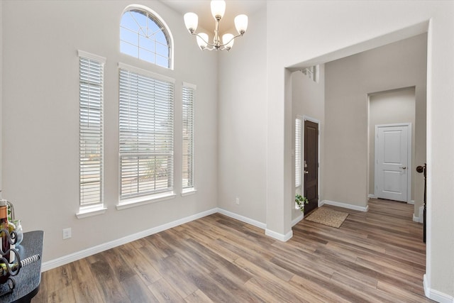 entrance foyer featuring a chandelier, light wood-style floors, a towering ceiling, and a healthy amount of sunlight