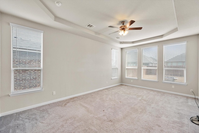 empty room featuring visible vents, a tray ceiling, baseboards, and light colored carpet