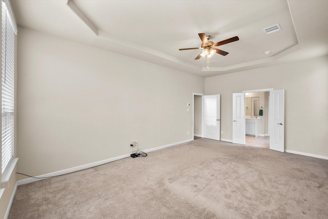 unfurnished bedroom with light colored carpet, visible vents, baseboards, a tray ceiling, and ensuite bath