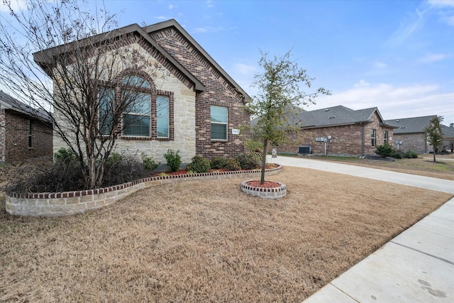 view of front facade with stone siding, a front yard, central AC, and brick siding