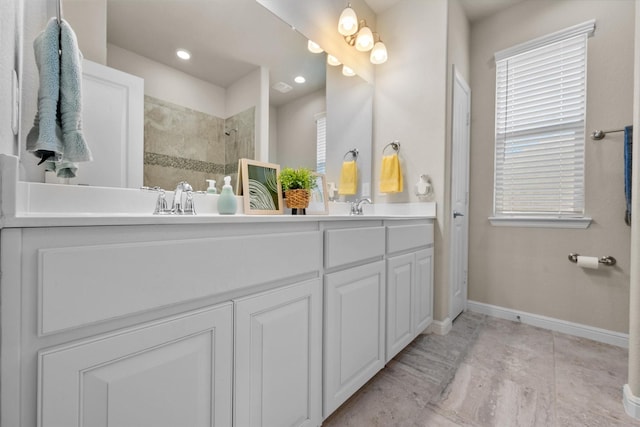 bathroom featuring a sink, double vanity, baseboards, and tiled shower