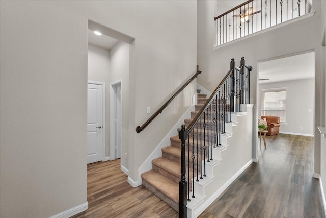 staircase featuring a high ceiling, baseboards, and wood finished floors