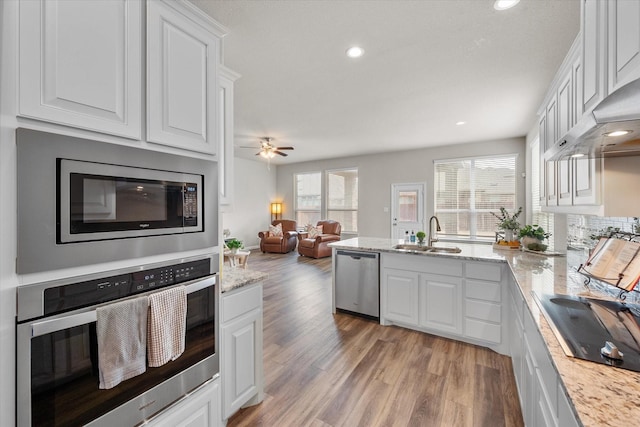 kitchen featuring light wood finished floors, appliances with stainless steel finishes, open floor plan, white cabinets, and a sink