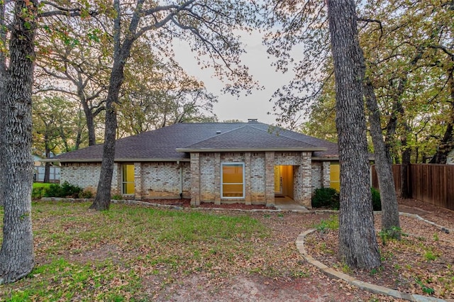 view of front of house with brick siding, a chimney, a shingled roof, and fence