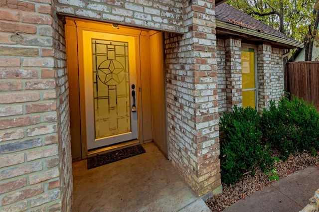 view of exterior entry with fence, brick siding, and a shingled roof