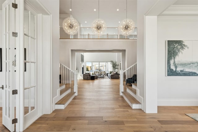 foyer entrance with light wood-type flooring, ornamental molding, a high ceiling, and a chandelier