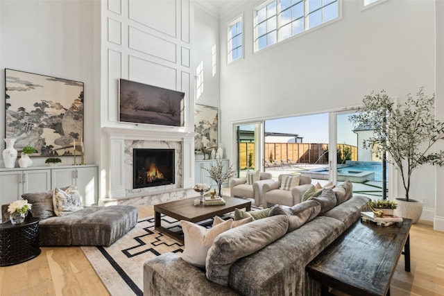 living room featuring light hardwood / wood-style flooring, a premium fireplace, crown molding, and a wealth of natural light