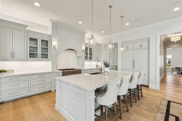 kitchen with range with two ovens, decorative light fixtures, ornamental molding, sink, and a kitchen island with sink