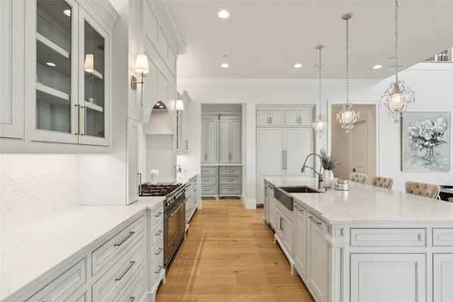 kitchen featuring double oven range, hanging light fixtures, an island with sink, sink, and a kitchen bar