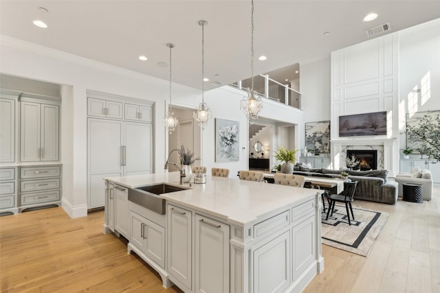 kitchen with hanging light fixtures, an island with sink, a premium fireplace, light hardwood / wood-style floors, and sink