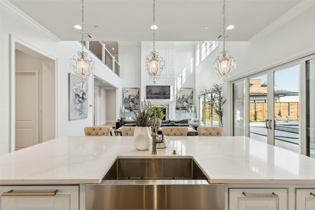 kitchen featuring an inviting chandelier, light stone counters, pendant lighting, crown molding, and white cabinets