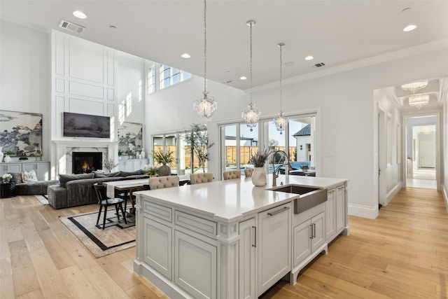 kitchen with an inviting chandelier, sink, pendant lighting, white cabinets, and a kitchen island with sink