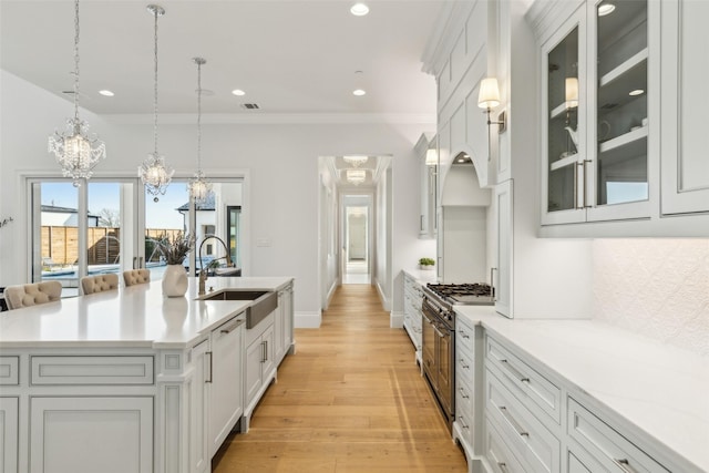 kitchen with white cabinetry, a center island with sink, decorative light fixtures, double oven range, and sink