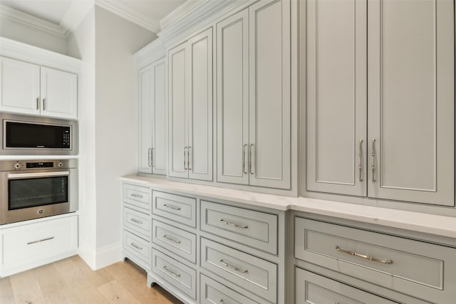 interior space featuring appliances with stainless steel finishes, light stone counters, white cabinets, light hardwood / wood-style floors, and ornamental molding