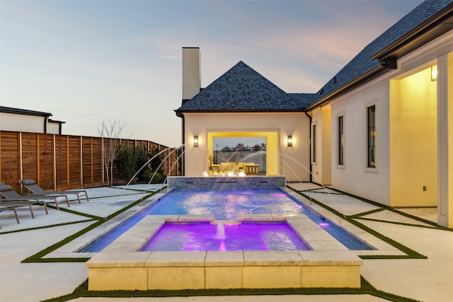 pool at dusk featuring a patio area and an in ground hot tub