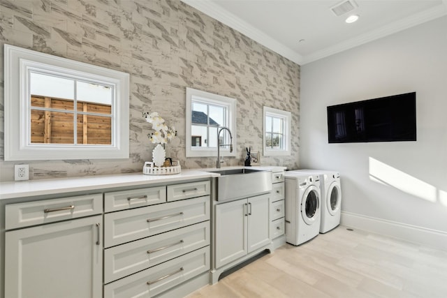 laundry area with washing machine and dryer, light hardwood / wood-style floors, crown molding, sink, and cabinets