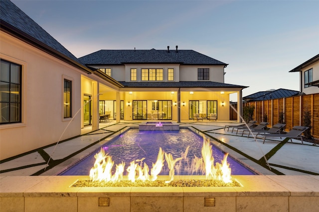 back house at dusk with a patio, a fire pit, and pool water feature