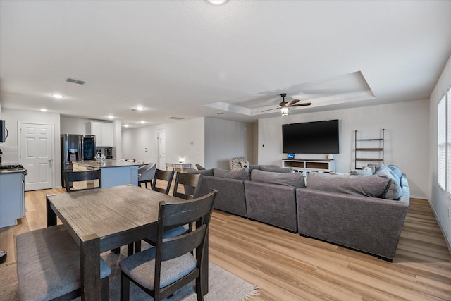 dining room with light wood-type flooring, ceiling fan, and a raised ceiling