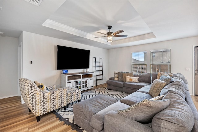 living room featuring a raised ceiling, crown molding, light hardwood / wood-style flooring, and ceiling fan