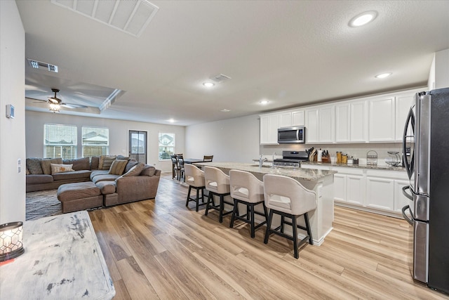 kitchen featuring light stone counters, white cabinetry, stainless steel appliances, an island with sink, and a breakfast bar area