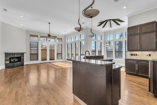 kitchen featuring ceiling fan, visible vents, open floor plan, hanging light fixtures, and a center island with sink