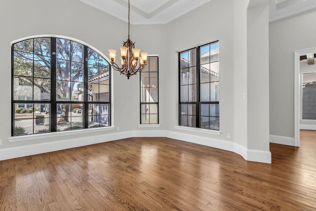 unfurnished dining area featuring ornamental molding, a chandelier, baseboards, and wood finished floors