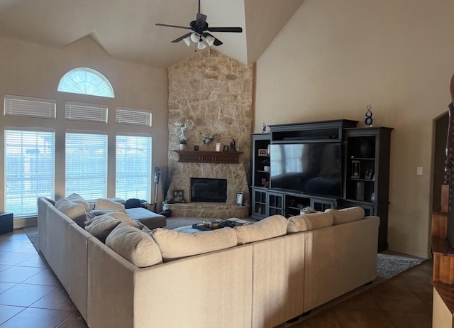 living area with high vaulted ceiling, light tile patterned flooring, a stone fireplace, and a ceiling fan