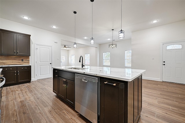 kitchen featuring hanging light fixtures, dark brown cabinets, stainless steel dishwasher, sink, and a kitchen island with sink