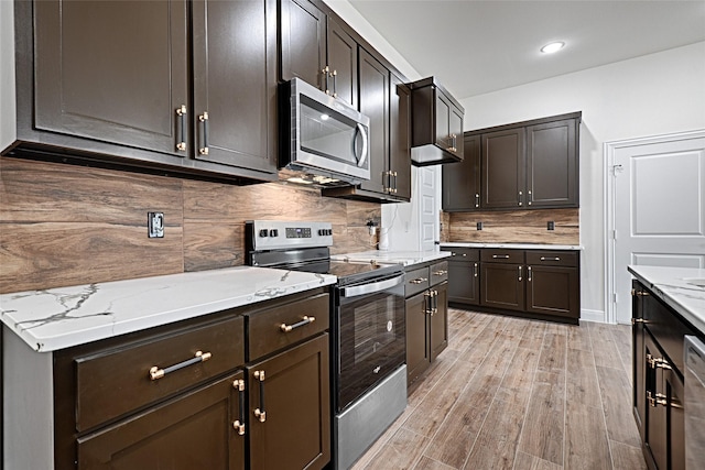 kitchen with light wood-type flooring, stainless steel appliances, dark brown cabinets, light stone countertops, and tasteful backsplash