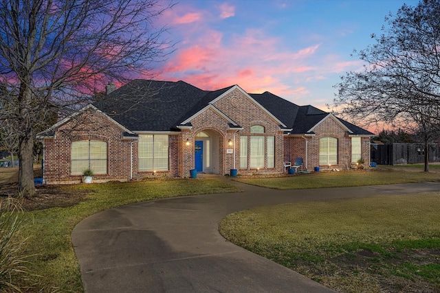 view of front of home with brick siding, fence, concrete driveway, roof with shingles, and a front yard