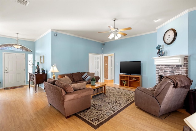 living room with a fireplace, ceiling fan, light hardwood / wood-style floors, and crown molding