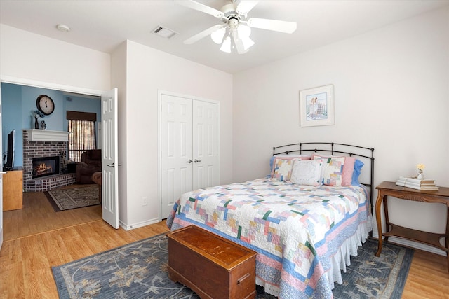 bedroom with a brick fireplace, hardwood / wood-style flooring, ceiling fan, and a closet